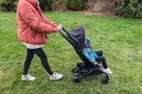 An individual pushing Joolz Aer+ Lightweight Stroller with a child seated in it across a grassy area outdoor scene