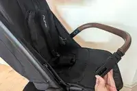 Nuna TRVL LX Stroller seat and armrest with a person holding the attachment point