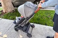 A person pushes the Uppababy Minu V3 Travel Stroller outside on a sidewalk