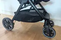 Closeup of a Nuna TRVL LX Stroller frame and wheels on a wooden floor