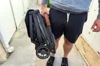 A person holds up the folded Uppababy Minu V3 Travel Stroller