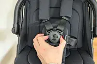 A person adjusts the buckle of a black harness on the Peg Perego Volo Compact Stroller