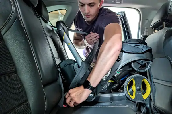 A person installs the Doona + Car Seat base in the back seat of a car