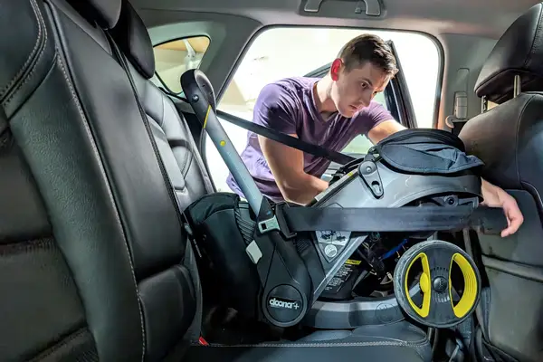 A person installs the Doona + Car Seat into the back seat of a car