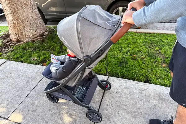 A person pushes the Uppababy Minu V3 Travel Stroller outside on a sidewalk