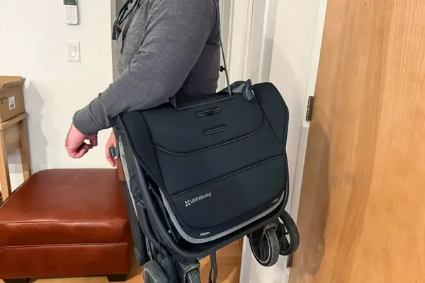 A person carries the Uppababy Minu V3 Travel Stroller with a strap