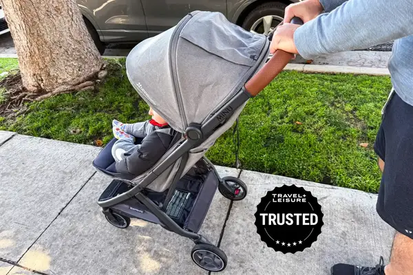 A child in Uppababy Minu V3 on a sidewalk accompanied by an adult pushing it