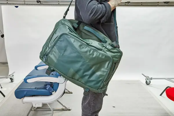 A person carries the Away The Outdoor Convertible Backpack 45L by the shoulder strap