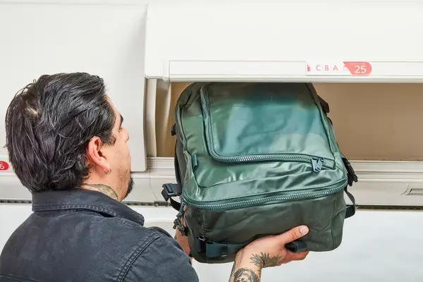 A person places the Away F.A.R. Convertible Backpack 45L into an overhead compartment