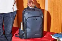 Person holding the Nomatic Travel Pack Laptop Bag 20L by the handle displayed on a red leather surface