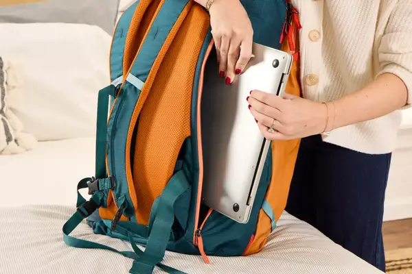 A person places a laptop into the Cotopaxi Allpa 42L Travel Pack