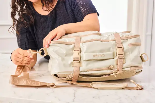 A person attaches a strap to the Calpak Terra 26L Laptop Duffel Backpack