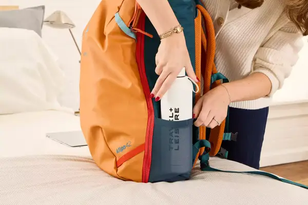 A person places a water bottle into the Cotopaxi Allpa 42L Travel Pack