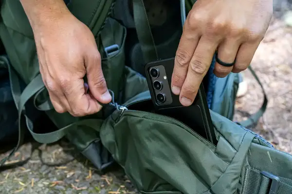 Hands placing a smartphone into a Osprey Kestrel 58L Men