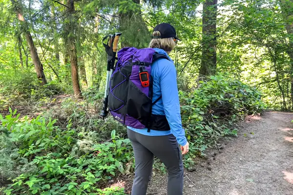 A person hiking on a forest trail with a ULA Equipment Circuit and trekking poles attached
