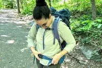 A person with a REI Co-op Traverse 60 Pack adjusting the strap outside on a path in the woods