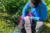 A person outdoors preparing gear from a ULA Equipment Circuit, with hiking equipment visible and greenery in the background