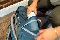 A hand placing a water bottle into the side pocket of a REI Co-op Traverse 60 Pack