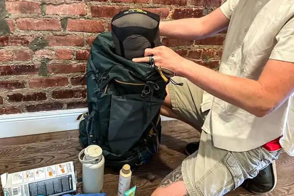 Person packing gear into a Gregory Katamai 55 - Hiking Backpack, camping equipment visible on the floor