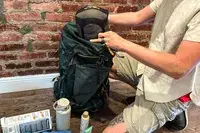 Person packing gear into a Gregory Katamai 55 - Hiking Backpack, camping equipment visible on the floor