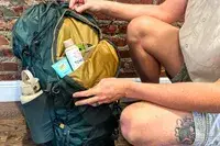 Person opening a Gregory Katamai 55 - Hiking Backpack containing toiletries and a water bottle sleeve