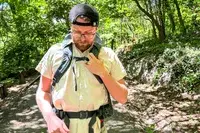 A person wearing a Gregory Katamai 55 - Hiking Backpack adjusts its strap while standing on a forest path