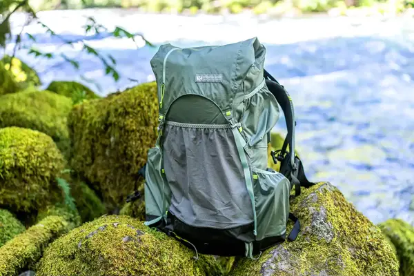 A Gossamer Gear Mariposa 60 Backpack placed on mossy rocks near a river