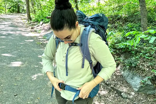 A person with a REI Co-op Traverse 60 Pack adjusting the strap outside on a path in the woods