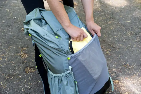 Hands placing an item in the pocket of a Gossamer Gear Mariposa 60 Backpack outdoors
