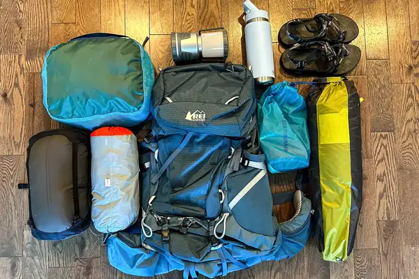 Camping equipment laid out, including a REI Co-op Traverse 60 Pack, rolled sleeping bag, water bottle, sandals, and other gear