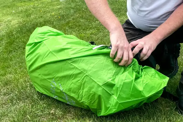 A person securing the strap of a Osprey Atmos AG LT 65 Pack on the grass