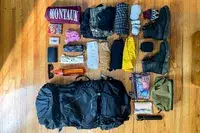 Assorted travel gear laid out on a wooden floor, including clothing, a Osprey Atmos AG 65 Men