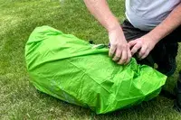 A person securing the strap of a Osprey Atmos AG LT 65 Pack on the grass
