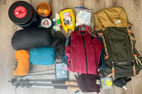 Equipment and supplies organized for an outdoor expedition, including a The North Face Trail Lite 50 Backpack, sleeping items, clothing, and other necessities