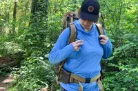Person hiking in a forest, wearing a The North Face Trail Lite 50 Backpack and a hat