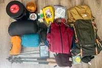 Equipment and supplies organized for an outdoor expedition, including a The North Face Trail Lite 50 Backpack, sleeping items, clothing, and other necessities