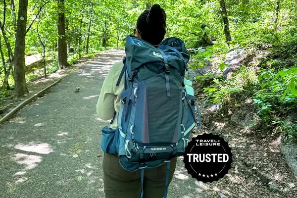 A person wearing a large backpack walking along a paved trail in the woods