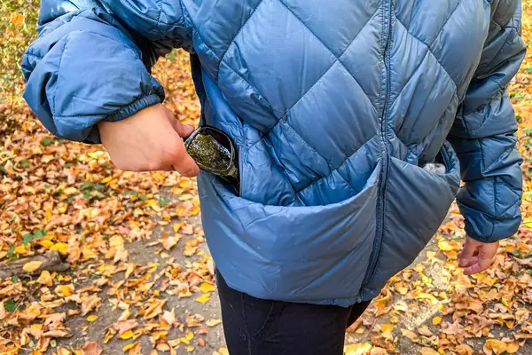 Person placing sunglasses in the pocket of Hikerkind Packable Down Puffer 0.1.