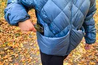 Person placing sunglasses in the pocket of Hikerkind Packable Down Puffer 0.1.