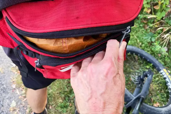 Close-up of a hand zipping a fanny pack containing a Cotopaxi Women
