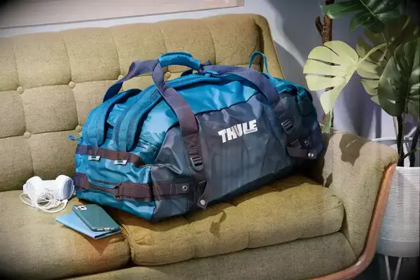 A person places a Calpak Terra 26L Laptop Duffel Backpack under the seat in front of them