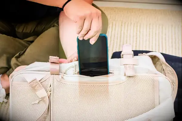 A person places a cell phone into the Calpak Terra 26L Laptop Duffel Backpack