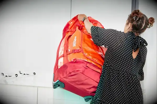 A person places a Calpak Terra 26L Laptop Duffel Backpack under the seat in front of them
