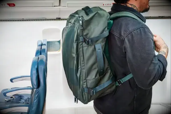 A person wears the Away The Outdoor Convertible Backpack 45L next to airplane seats