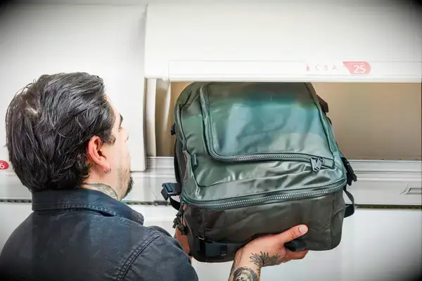 A person places the Away The Outdoor Convertible Backpack 45L into an overhead compartment
