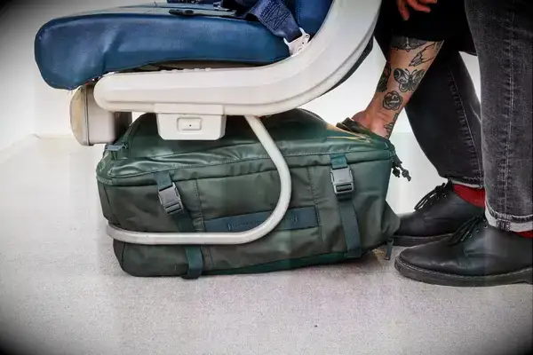 Hand places the Away The Outdoor Convertible Backpack 45L under a seat