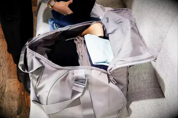 A person packing clothes into the Dagne Dover Lagos Convertible Duffle Bag