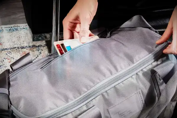 A person putting a wallet into the zipper pocket of the Dagne Dover Lagos Convertible Duffle Bag