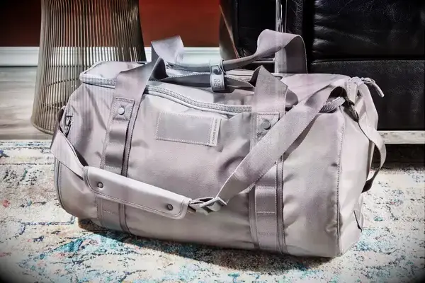 Dagne Dover Lagos Convertible Duffle Bag staged on a rug in front of a chair and side table