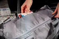 A person putting a wallet into the zipper pocket of the Dagne Dover Lagos Convertible Duffle Bag